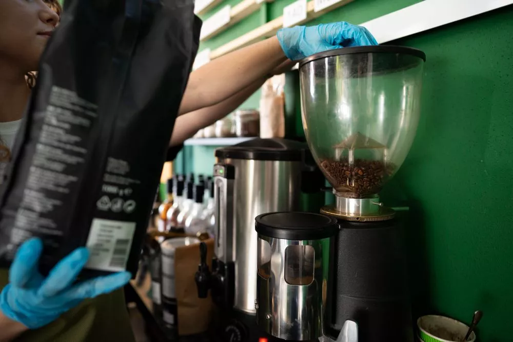 barista menuang biji kopi untuk digiling di sebuah kedai kopi